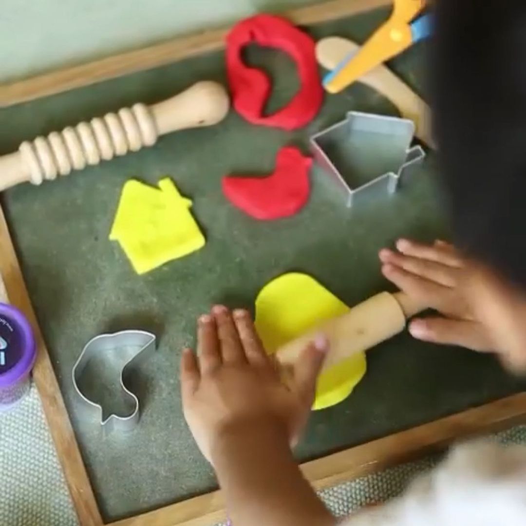 Child using rolling pin to roll the clay and dough and play with cutter