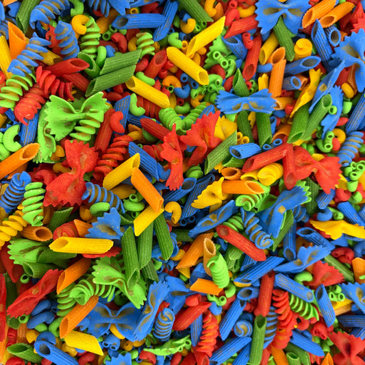 Colorful assortment of pasta shapes including fusilli, rotini, and other types. A colorful sensory bin filled with vibrant, multi-patterned pasta pieces in red, yellow, green, and blue, perfect for fine motor skill development and creative play for toddlers.
