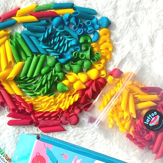 A colorful sensory bin filled with vibrant, multi-patterned pasta pieces in red, yellow, green, and blue, perfect for fine motor skill development and creative play for toddlers.